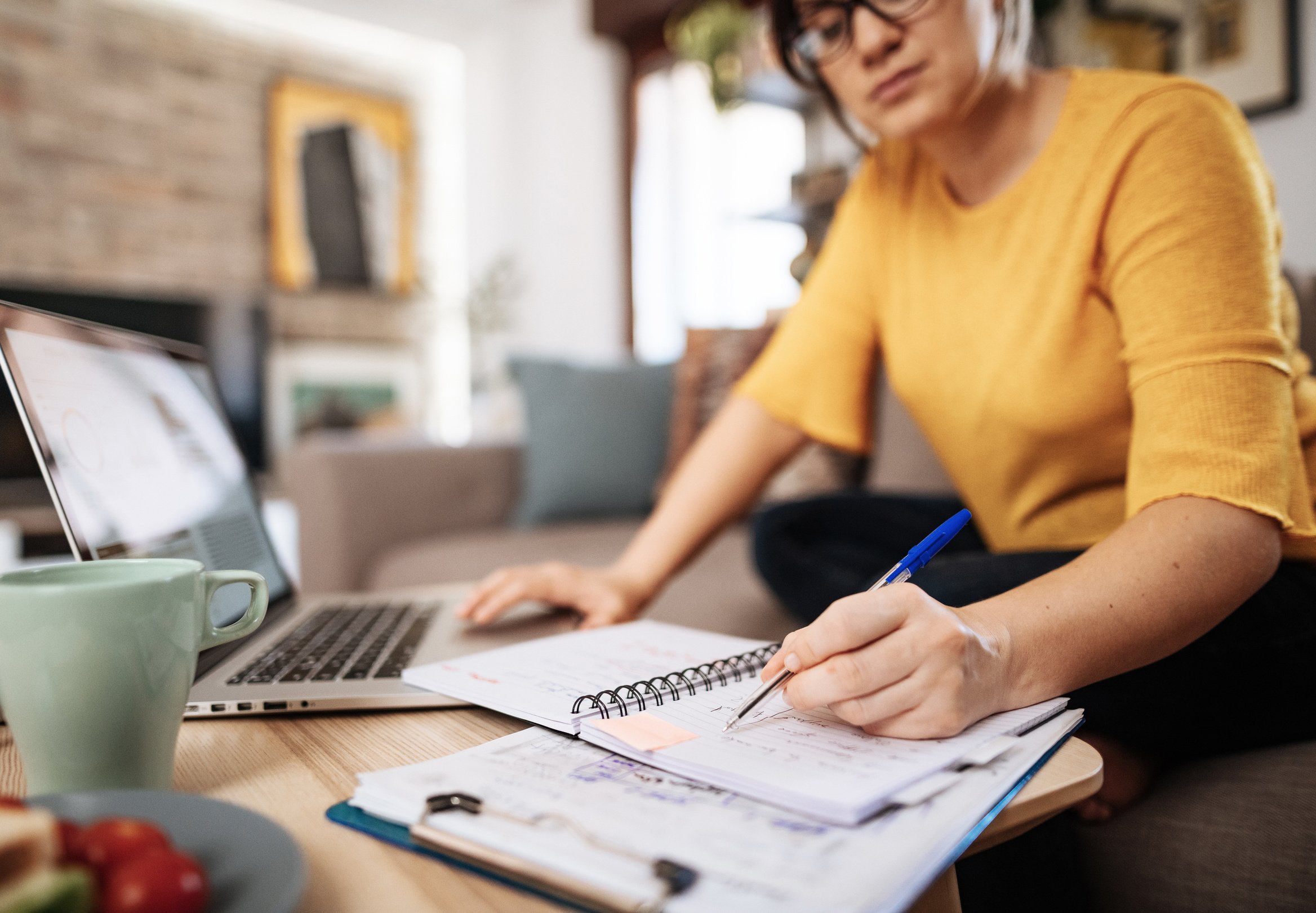 Woman working from home on laptop and taking notes during online meeting